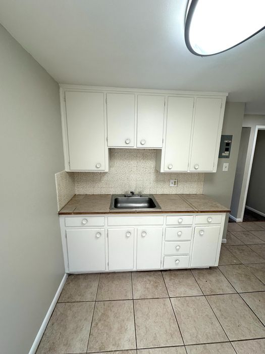 Bright kitchen featuring sleek white cabinetry, elegant tile flooring, and a stainless steel sink, perfect for modern living.