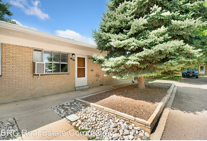 Charming single-story home with a brick exterior and front garden featuring a large, lush evergreen tree.