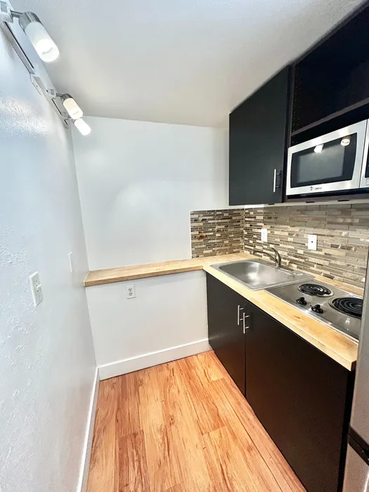 Chic kitchen nook featuring sleek black cabinets, modern appliances, and elegant wood flooring.