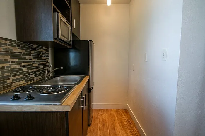 Compact modern kitchen with sleek dark cabinetry, stainless steel appliances, and stylish tile backsplash.