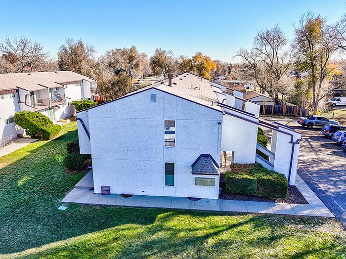 Charming apartment complex with well-maintained lawns, inviting pathways, and ample parking, surrounded by lush greenery on a bright sunny day.