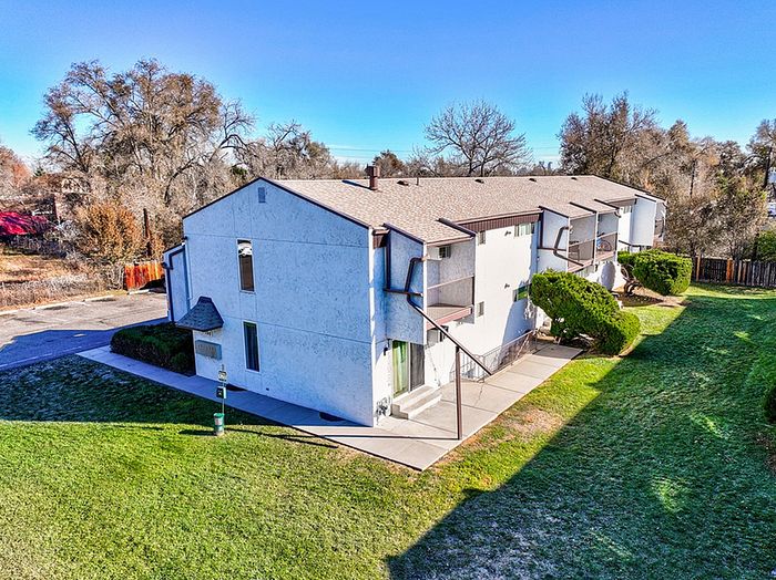 Charming two-story apartment building surrounded by lush greenery and vibrant trees, offering a tranquil living area with ample outdoor space.