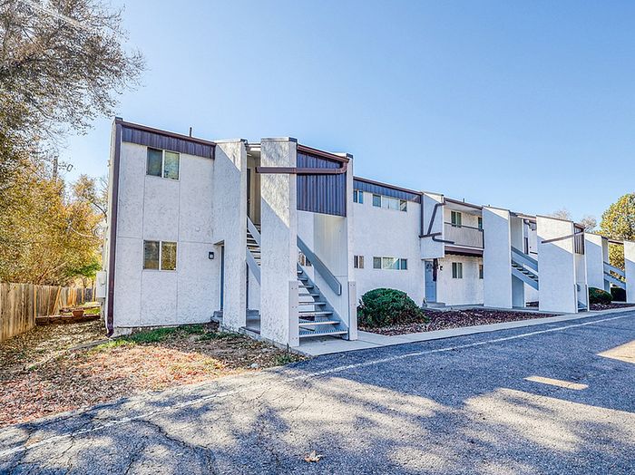 Charming modern apartment complex with white facade and multiple staircases, nestled in a serene wooded area.