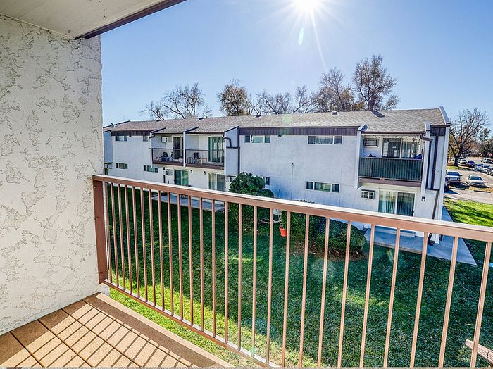 Charming apartment balcony view showcasing a sunny, serene landscape with manicured lawns and modern nearby buildings.