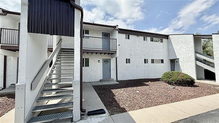 Charming apartment exterior with contemporary design, featuring white walls, stylish gray doors, and outdoor stairway access.