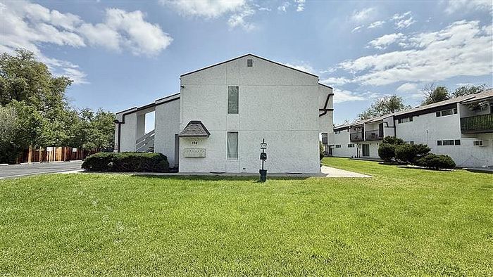 Charming apartment complex with fresh white fa&ccedil;ade, nestled in a lush green landscape under a bright blue sky.