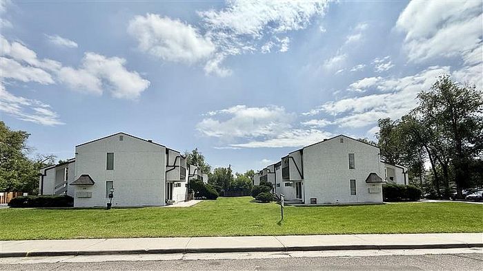 Charming residential complex featuring picturesque white buildings with distinct architectural design, surrounded by lush green lawns under a bright, sunny sky.
