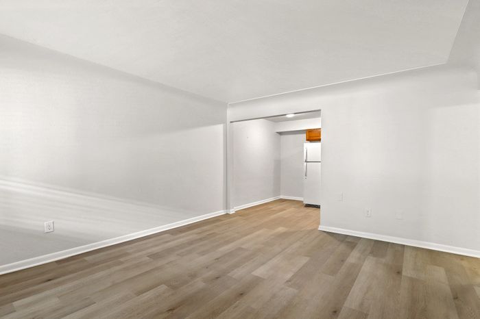 Bright and spacious open-plan living area with sleek laminate wood flooring and crisp white walls, leading to a cozy kitchen nook with modern appliances.