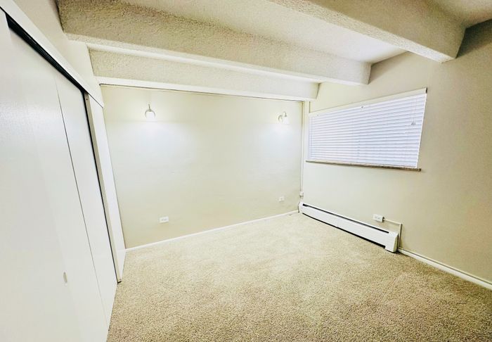Bright and cozy room with soft carpet flooring, modern wall lights, and a large window inviting natural light.