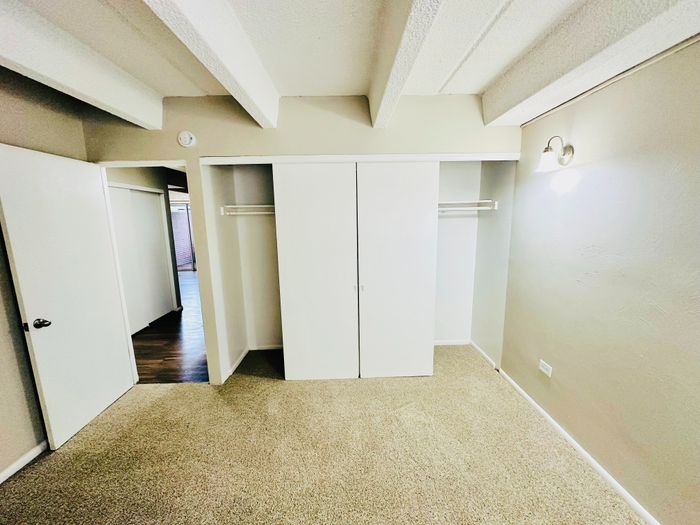 Bright bedroom with plush carpet, sliding closet doors, and exposed ceiling beams, offering a cozy and inviting space.