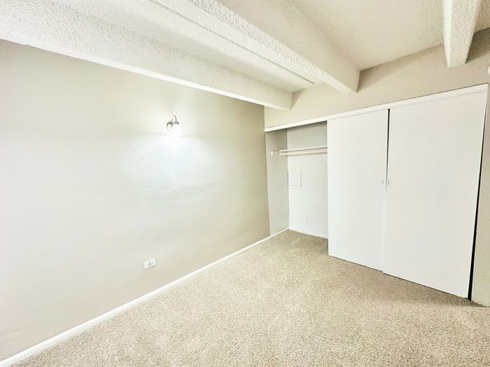 Bright and airy bedroom featuring soft carpet flooring, modern light fixture, and spacious closet with sliding doors.