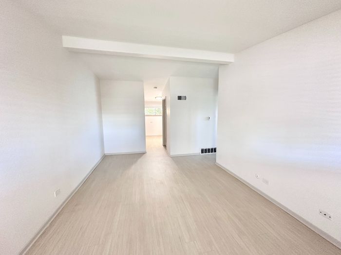 Bright, spacious hallway with modern light flooring and clean white walls, leading to a cozy living area.