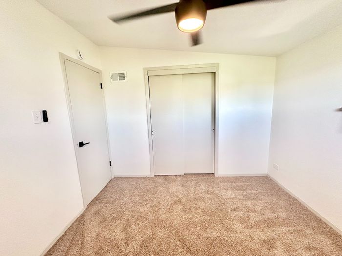 Bright, carpeted room with modern ceiling fan and sleek closet doors, perfect for customization and comfort.