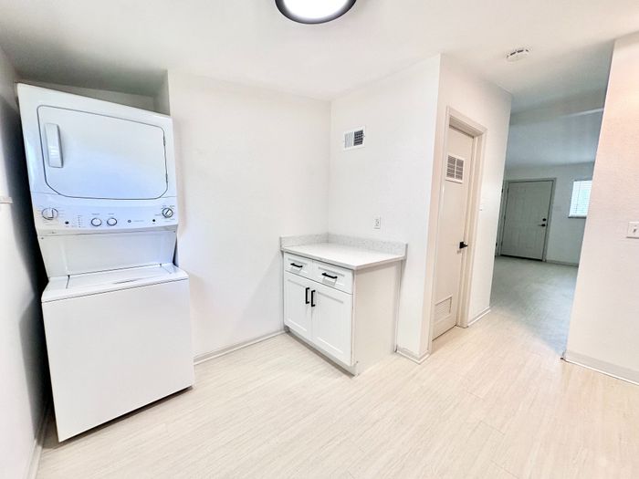 Bright and modern laundry area with stacked washer and dryer, sleek white cabinetry, and elegant flooring in a spacious apartment.