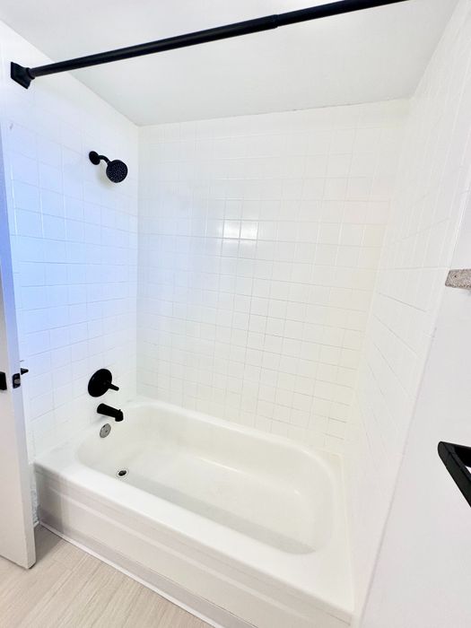 Pristine bathroom featuring a sleek white bathtub, modern black fixtures, and elegant tile walls.