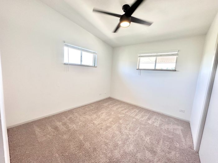 Bright and airy bedroom with soft carpeting, modern ceiling fan, and ample natural light from dual windows, offering a serene retreat.