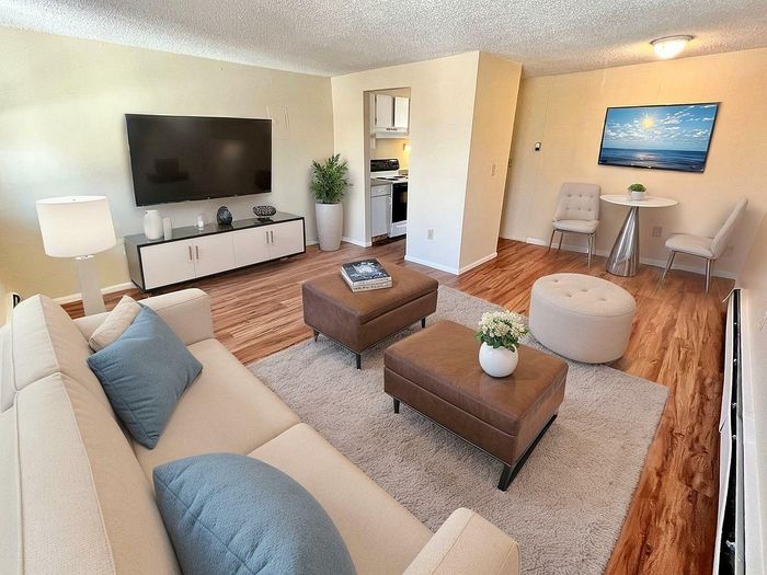 Bright and modern living room with stylish decor, featuring a large wall-mounted TV, cozy beige sofa, and elegant wood flooring.