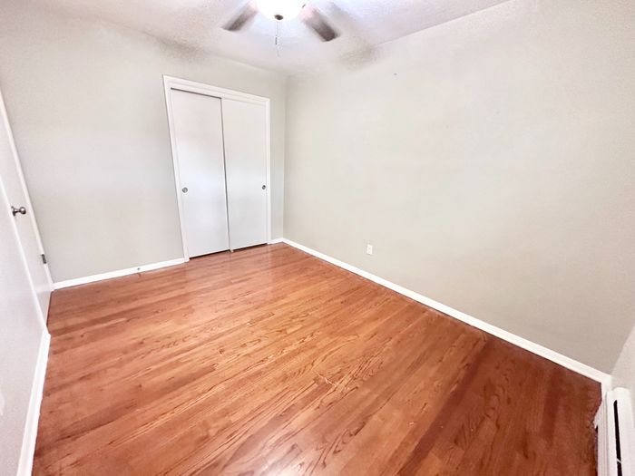 Bright, airy room with elegant hardwood floors and a ceiling fan, perfect for a cozy bedroom or home office.