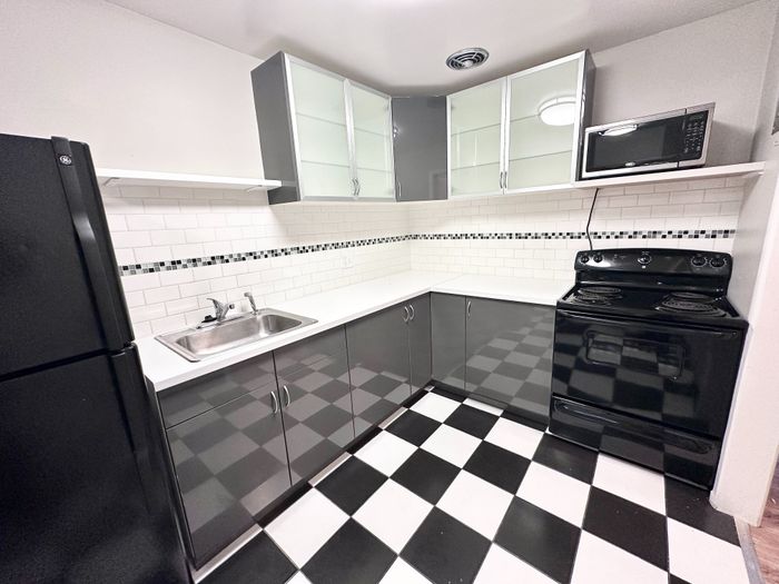 Modern kitchen with sleek black and white cabinetry, chic checkered floor, and contemporary appliances.