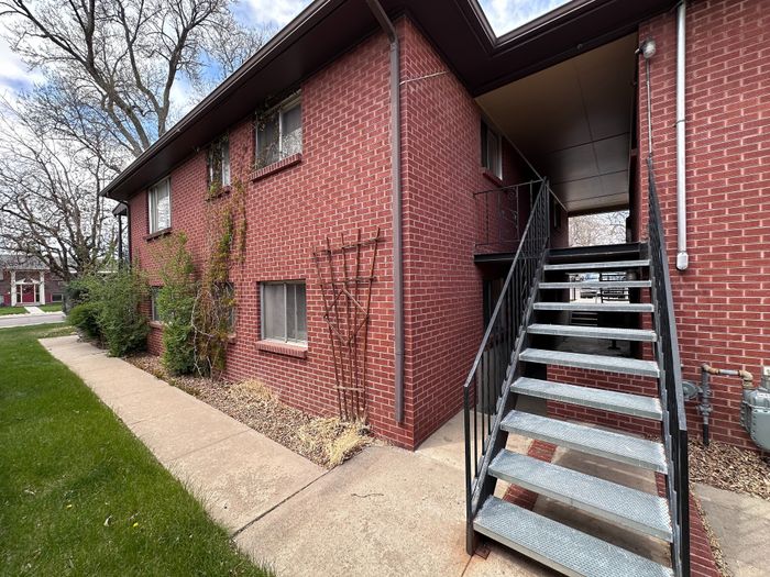 Charming brick apartment entrance with modern outdoor staircase and lush landscaping for a welcoming atmosphere.