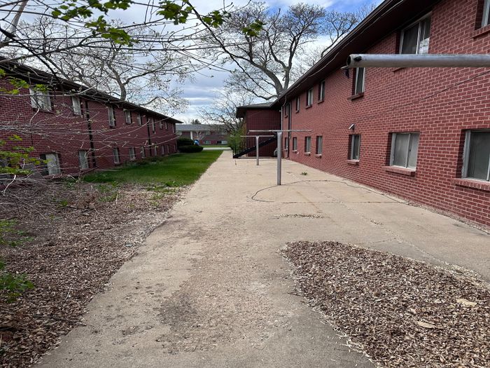Charming red brick apartment building with lush green surroundings and a peaceful walkway, perfect for tranquil living.