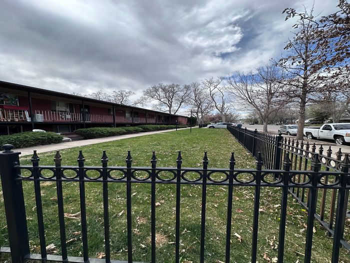 Charming apartment exterior with lush green lawn, elegant black iron fencing, and inviting pathways under a picturesque sky.