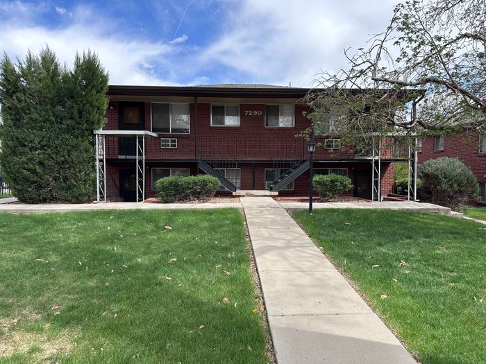 Charming brick apartment building with a modern exterior, lush green lawn, and inviting pathway.