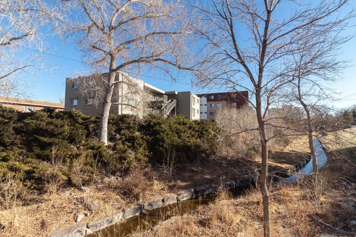 Charming apartment complex nestled among lush greenery with a serene creek and expansive blue sky view.