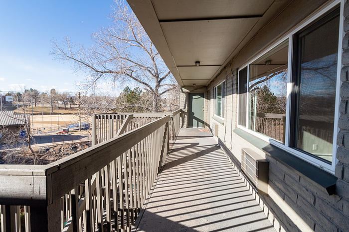 Charming apartment balcony with scenic view of a sunlit park and tree-lined horizon, perfect for relaxing outdoors.