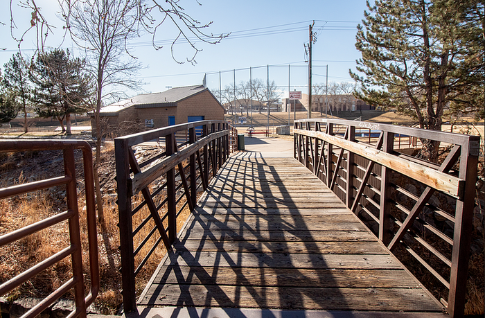 Charming pedestrian bridge leading to a serene park area, with rustic wooden planks and metal railings, perfect for nature walks and outdoor relaxation.