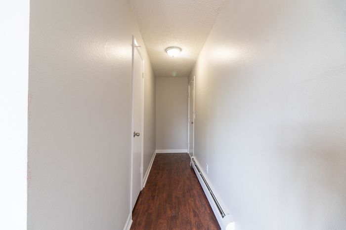 Inviting apartment hallway with modern wooden flooring and soft lighting, leading to multiple doors.