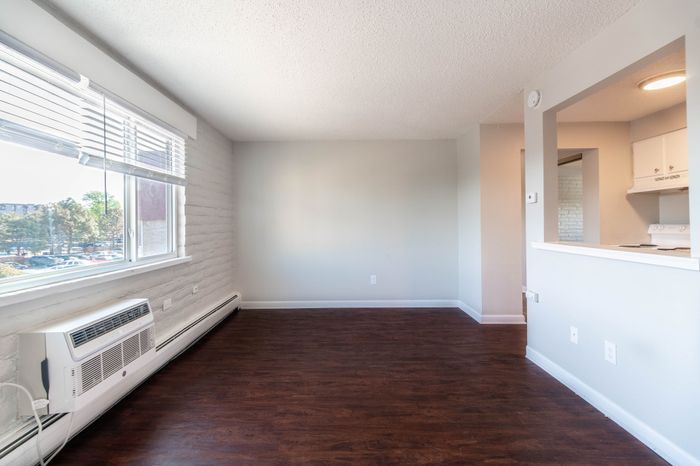 Bright and airy living area with large windows, sleek hardwood floors, and a cozy open kitchen design.