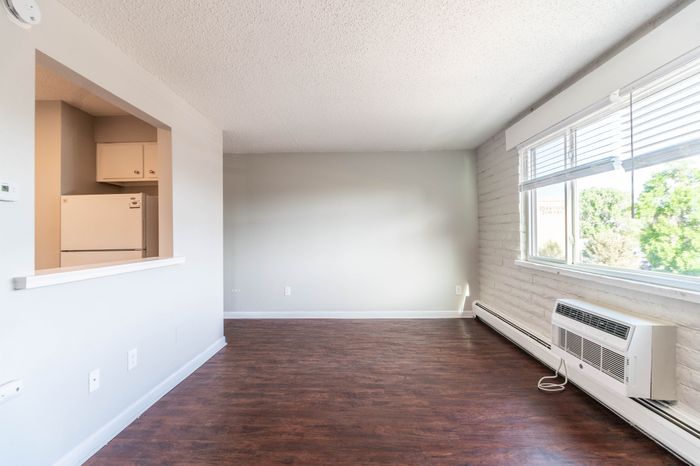 Bright living area with elegant wood flooring and large window offering garden views, adjacent to a cozy kitchen space.