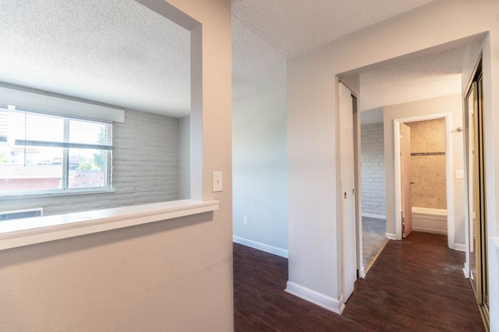 Inviting apartment hallway with elegant laminate flooring and bright natural light, featuring a glimpse into a cozy bathroom.