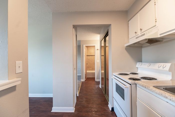 Bright and inviting apartment hallway leading to a cozy bathroom, featuring gleaming hardwood floors and modern kitchen amenities with elegant white cabinetry.