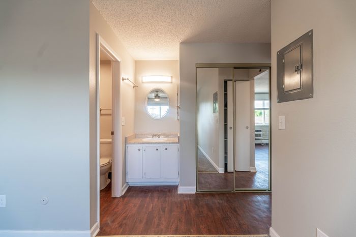 Modern apartment interior featuring bright bathroom with stylish vanity and mirror, mirrored closet doors, and elegant wood flooring, creating a welcoming and airy atmosphere.
