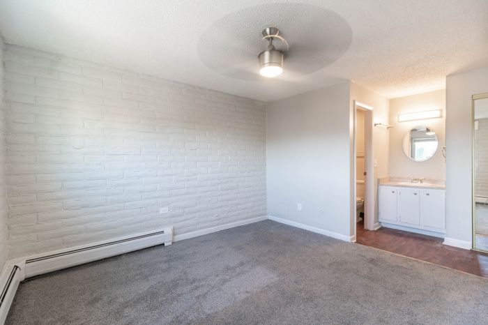 Bright and cozy bedroom with soft carpet flooring, modern ceiling fan, and an elegant vanity area exuding comfort and style.