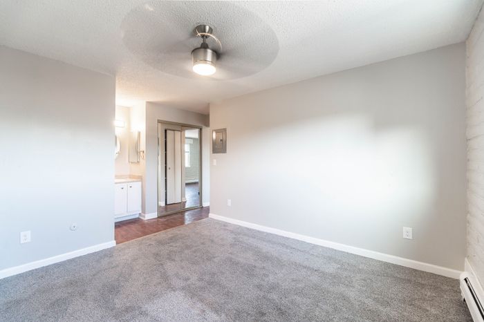 Bright and airy living space with modern ceiling fixture, beige carpet, and built-in storage, leading to a stylish bathroom with sleek fixtures.