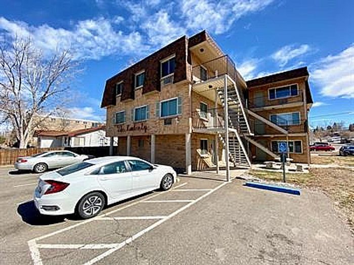 Charming three-story apartment building with spacious balconies, ample parking, and a bright blue sky backdrop.