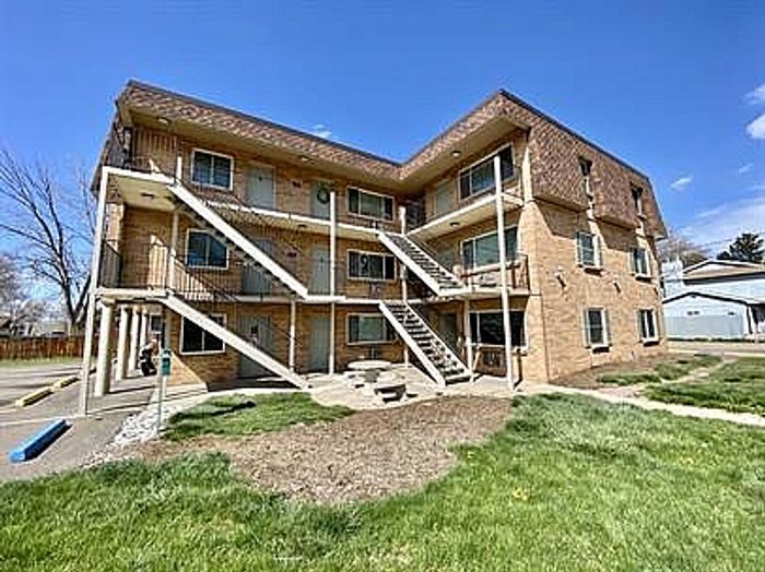 Charming brick apartment building with white staircases, surrounded by lush green lawns, basking under a clear blue sky.