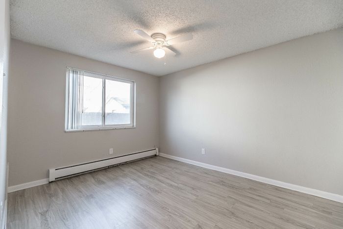 Bright and airy bedroom featuring sleek wood flooring, a large window, and a modern ceiling fan, perfect for a cozy living space.