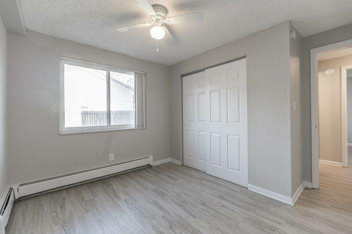 Bright and airy bedroom featuring large window, sleek closet doors, modern ceiling fan, and elegant wood-style flooring.