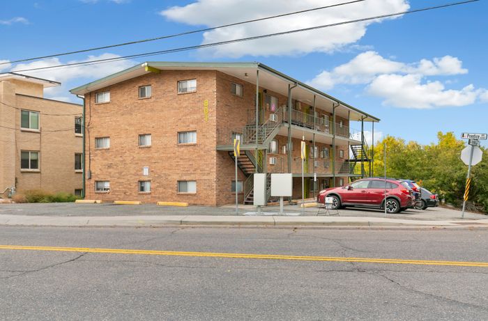Charming three-story brick apartment building with convenient outdoor staircases and ample parking, set against a bright blue sky.