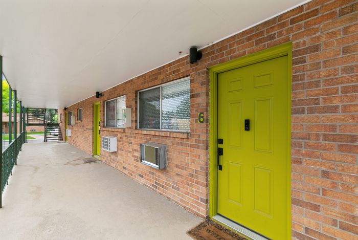 Charming apartment entrance with a vibrant green door against a classic brick facade, offering welcome warmth and character.