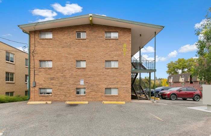 Charming brick apartment building with outdoor staircase, ample parking, and clear blue skies.