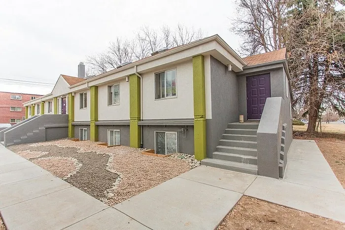 Charming modern apartment building with vibrant accents and inviting entrance, surrounded by a tidy xeriscape garden.