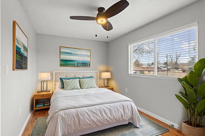 Bright bedroom with elegant decor, featuring a cozy bed, artistic wall paintings, and a large window offering serene views.