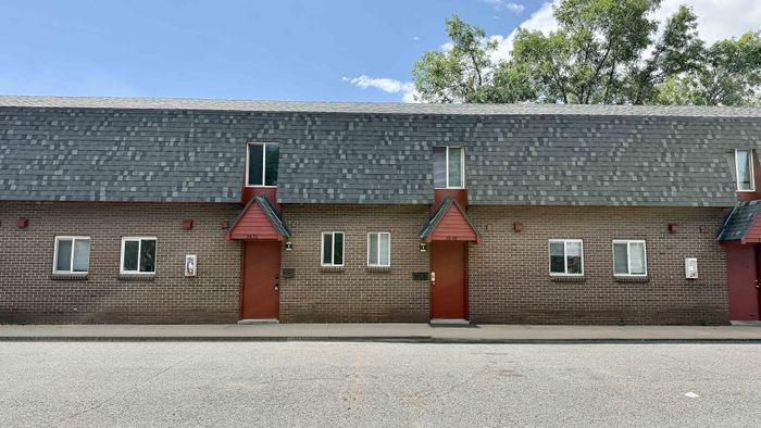Charming townhouse exterior with red brick facade, unique A-frame windows, and inviting red doors.