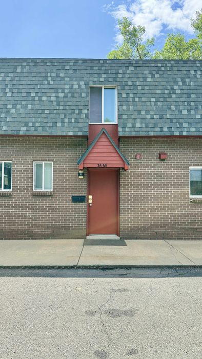 Charming brick townhouse facade with a red door, slate gabled roof, and modern windows against a clear blue sky.