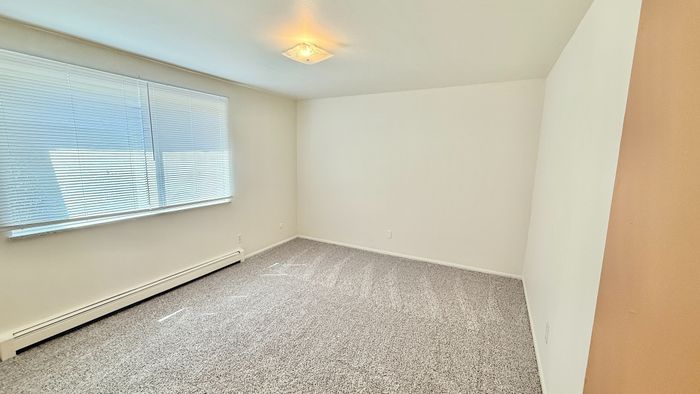 Bright and spacious bedroom with large window, plush carpeting, and natural light creating a warm and inviting atmosphere.